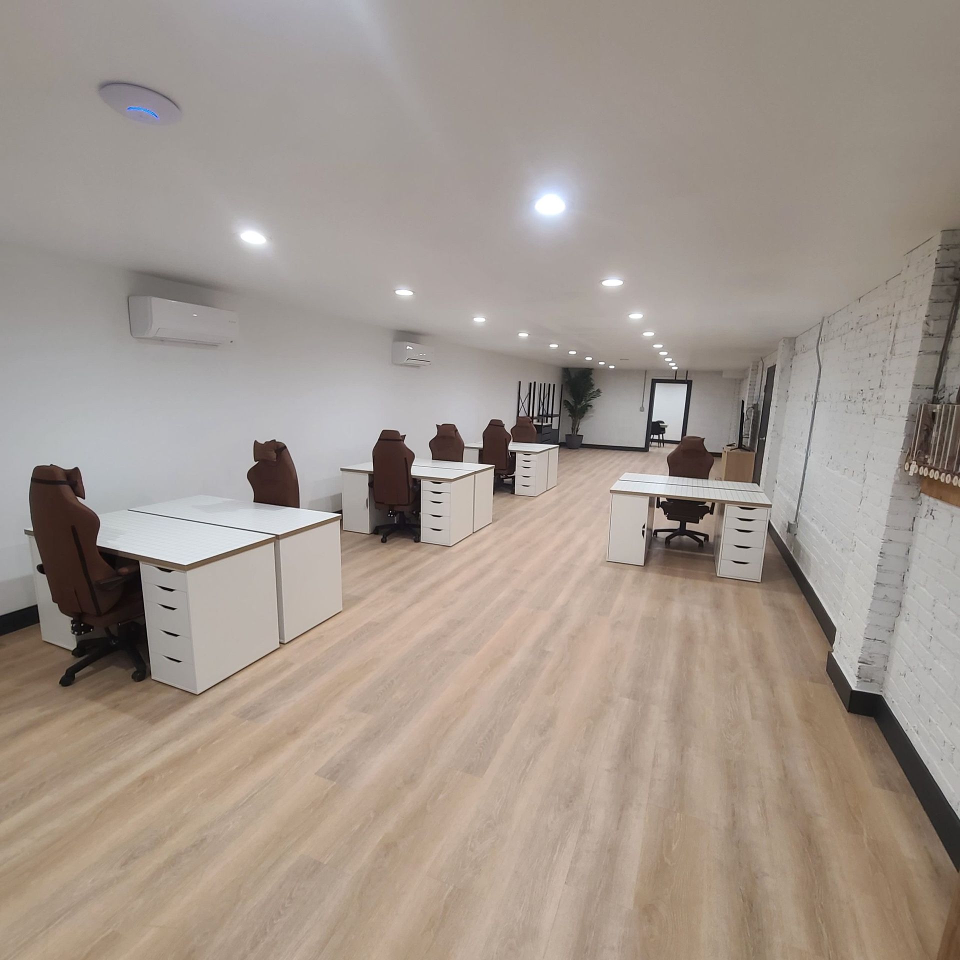 Office space with white desks, brown chairs, wood flooring, and exposed brick wall.