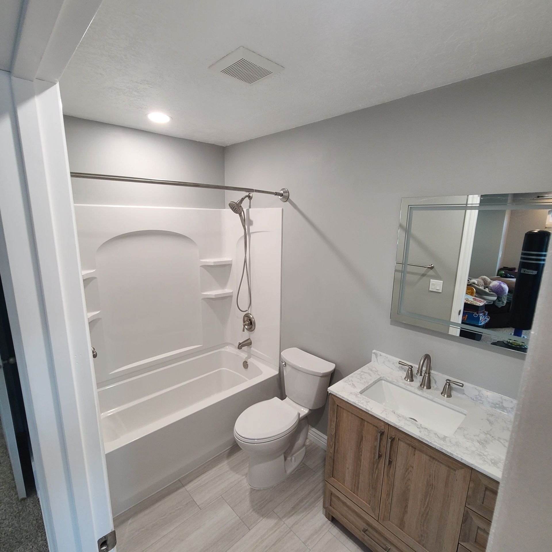 Bathroom with white tub/shower, toilet, wood vanity, and gray walls.