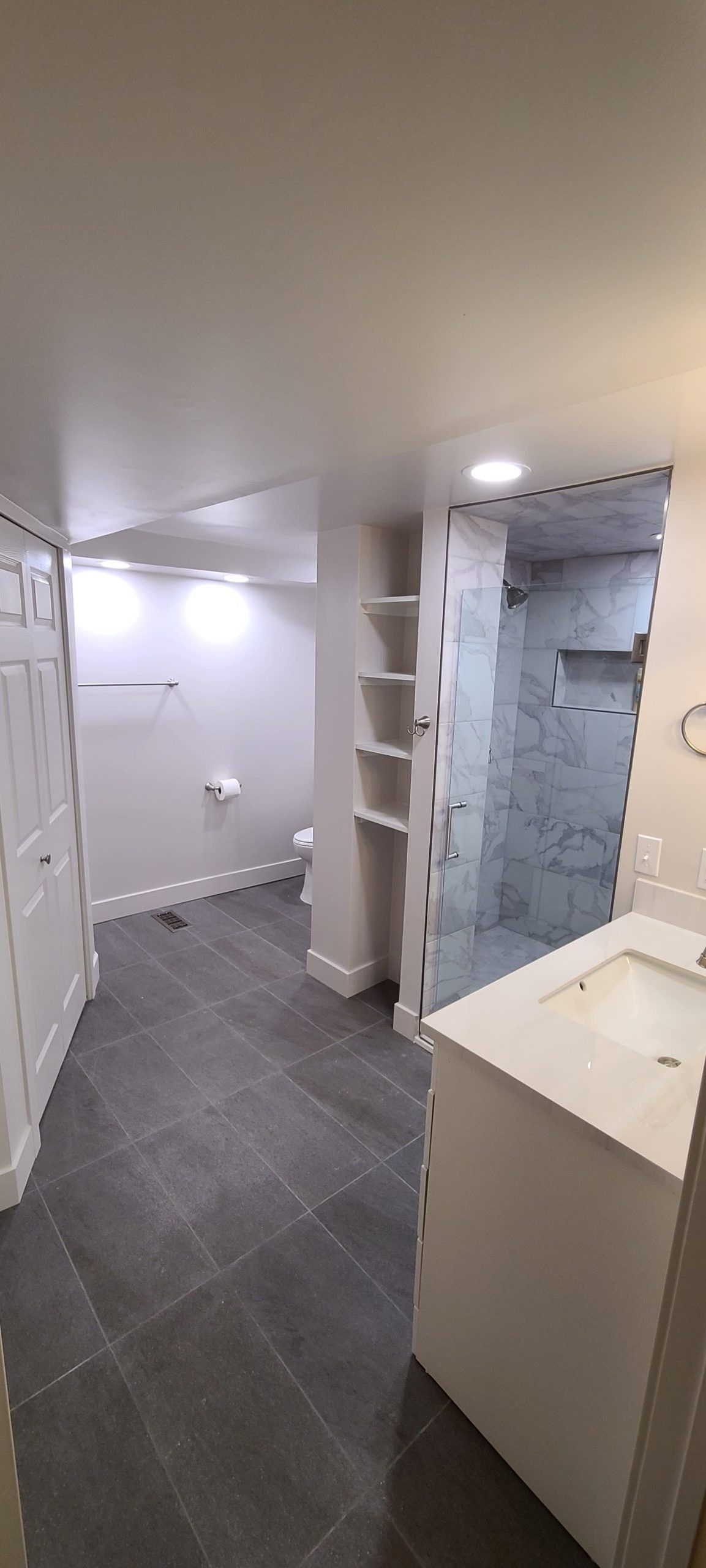 Bathroom with gray tile, white walls, a shower, shelves, and a sink.