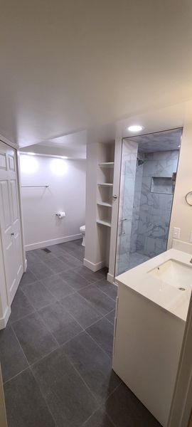 Bathroom with white cabinets, gray tile floor, and a marble shower.