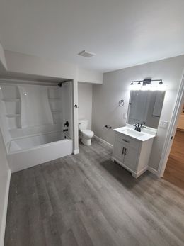 Bathroom with white tub, vanity, and toilet. Gray flooring and walls.