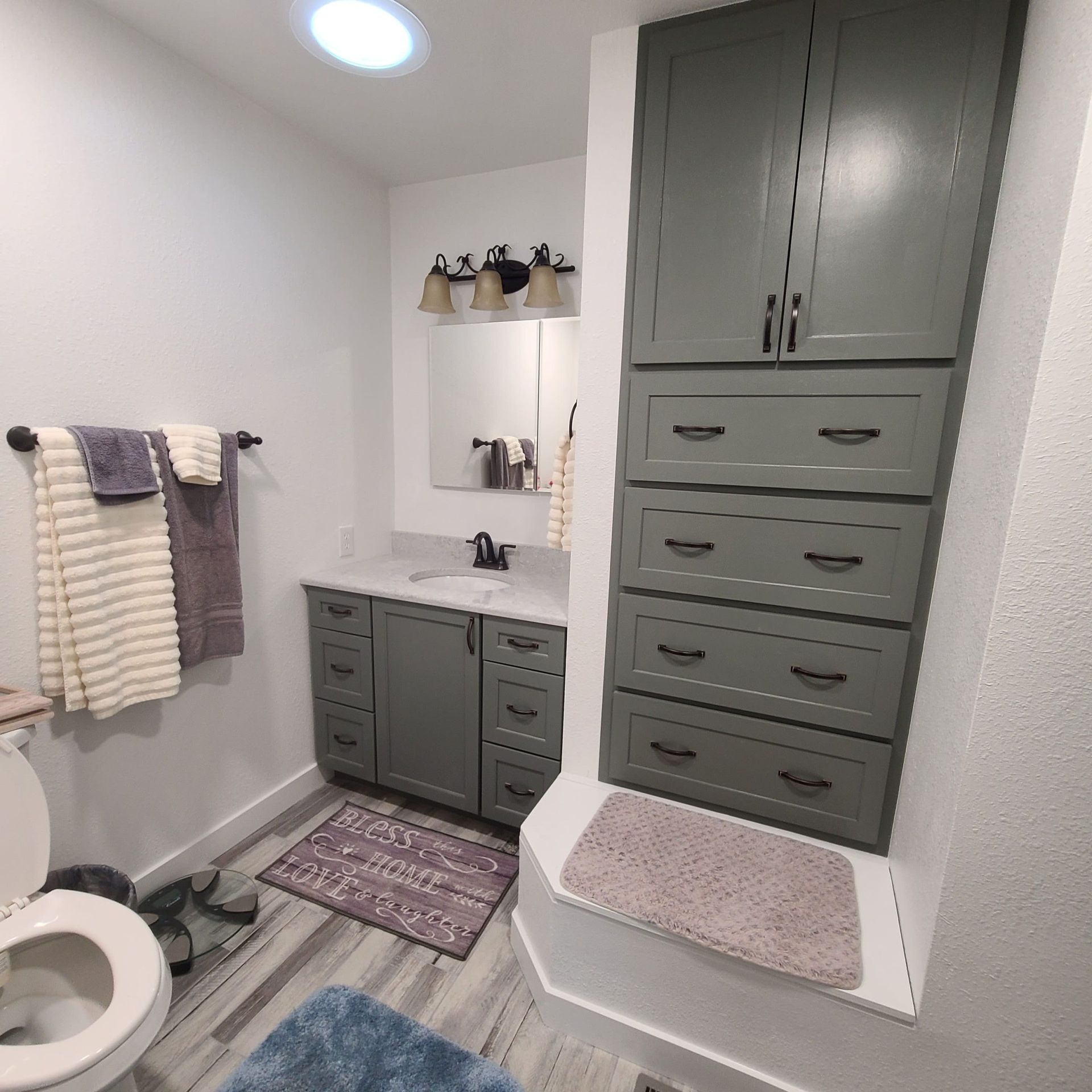A bathroom with gray cabinets, towels, and a toilet. The space is lit by a ceiling light.