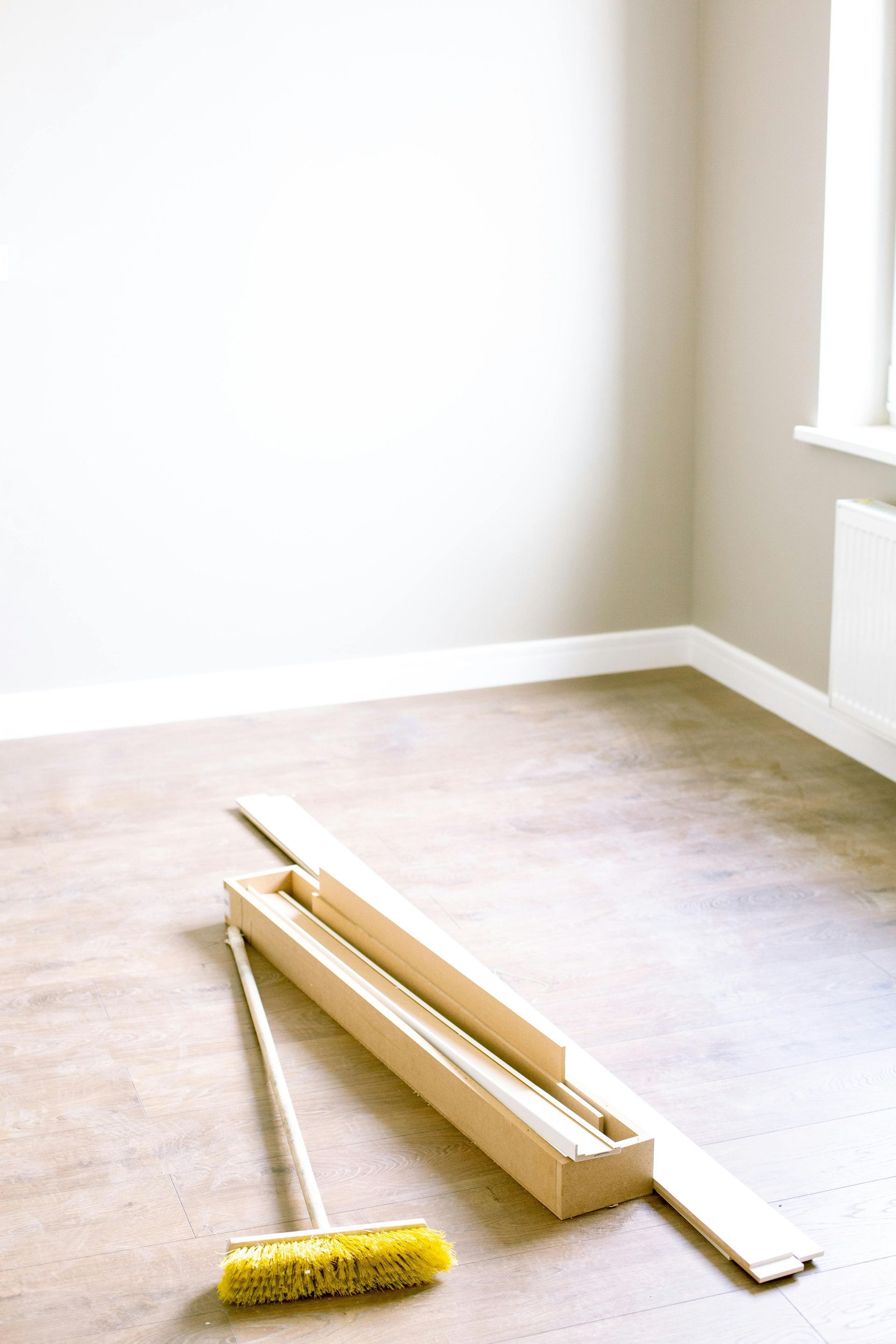 Empty room with light brown flooring, tan walls, and a broom and wooden molding on the floor.
