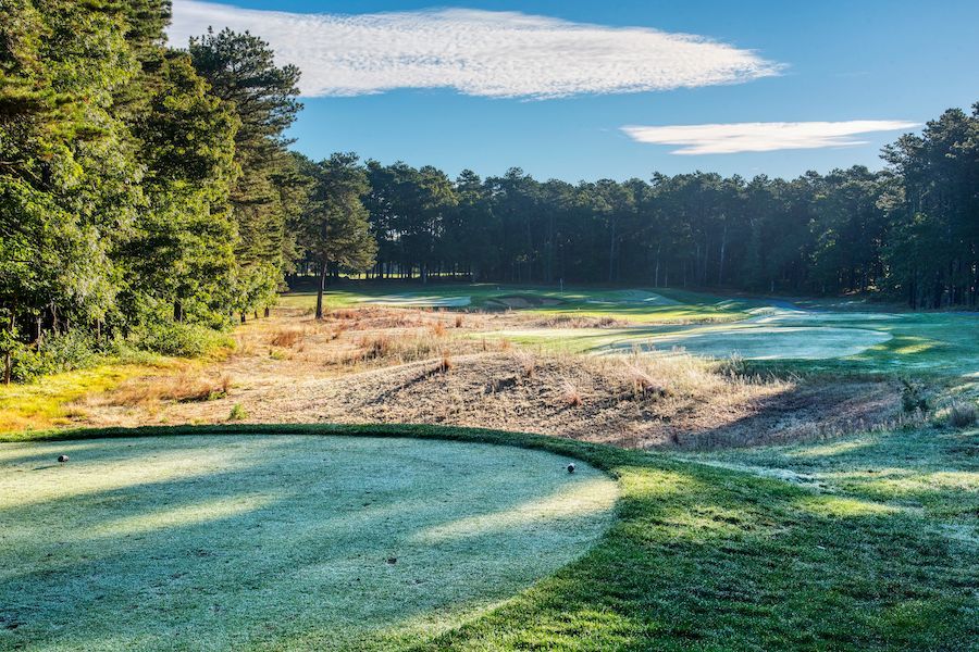 A golf course with a green and trees in the background on a sunny day.