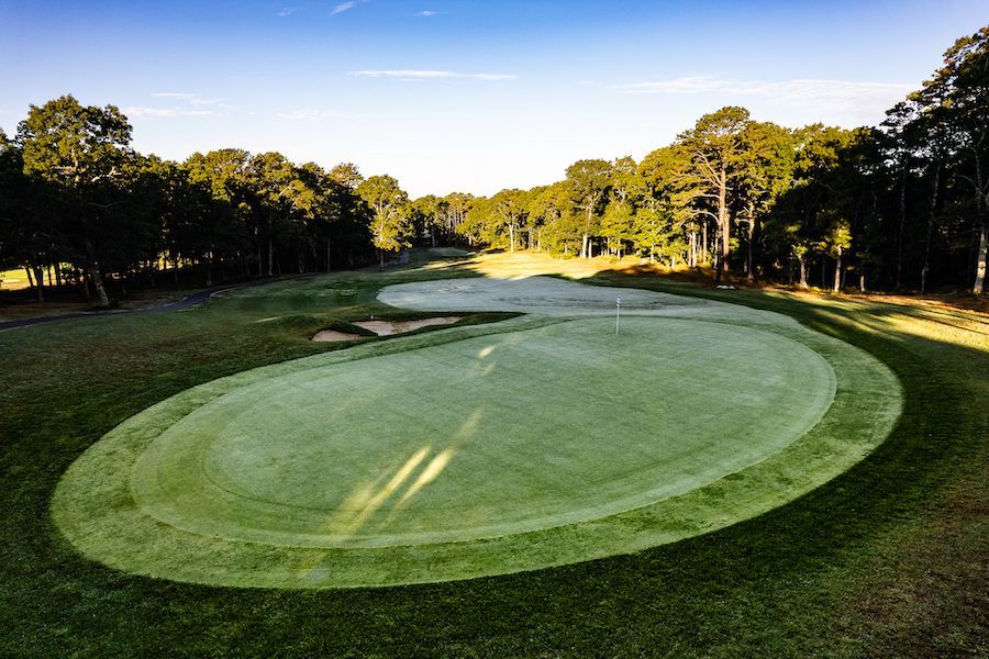 A golf course with a green and trees in the background