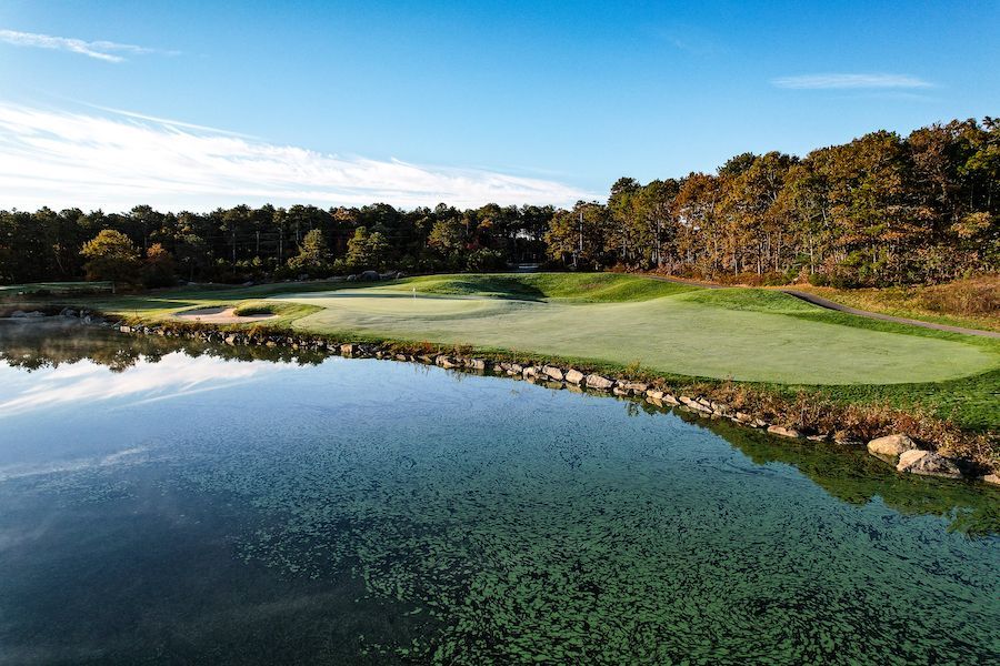 An aerial view of a golf course with a lake in the foreground and trees in the background.
