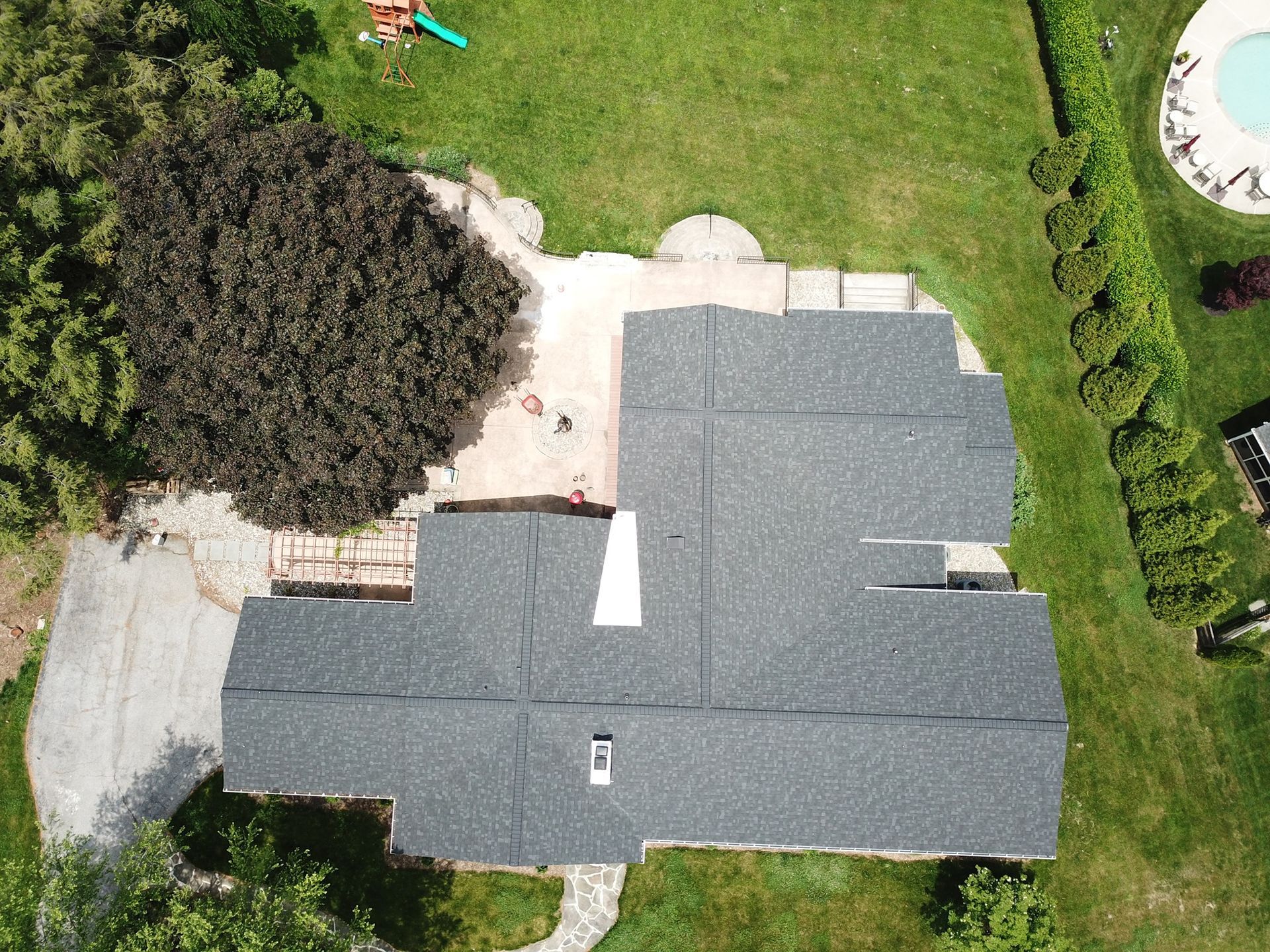 Overhead view of a house with a dark gray roof, surrounded by green grass and a small swimming pool.