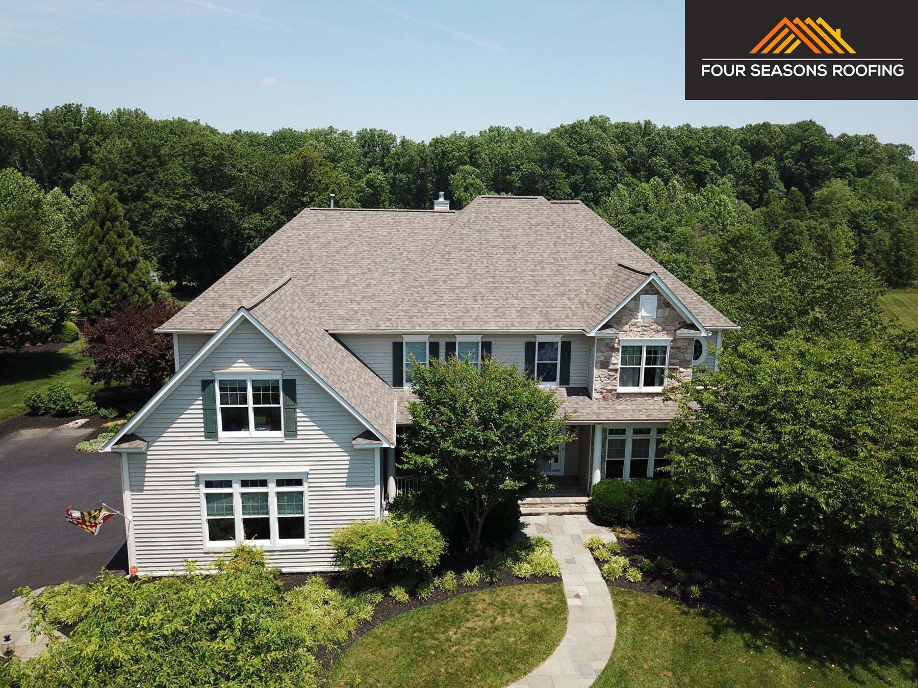 House with gray roof, stone accents, surrounded by trees. Four Seasons Roofing logo in the corner.