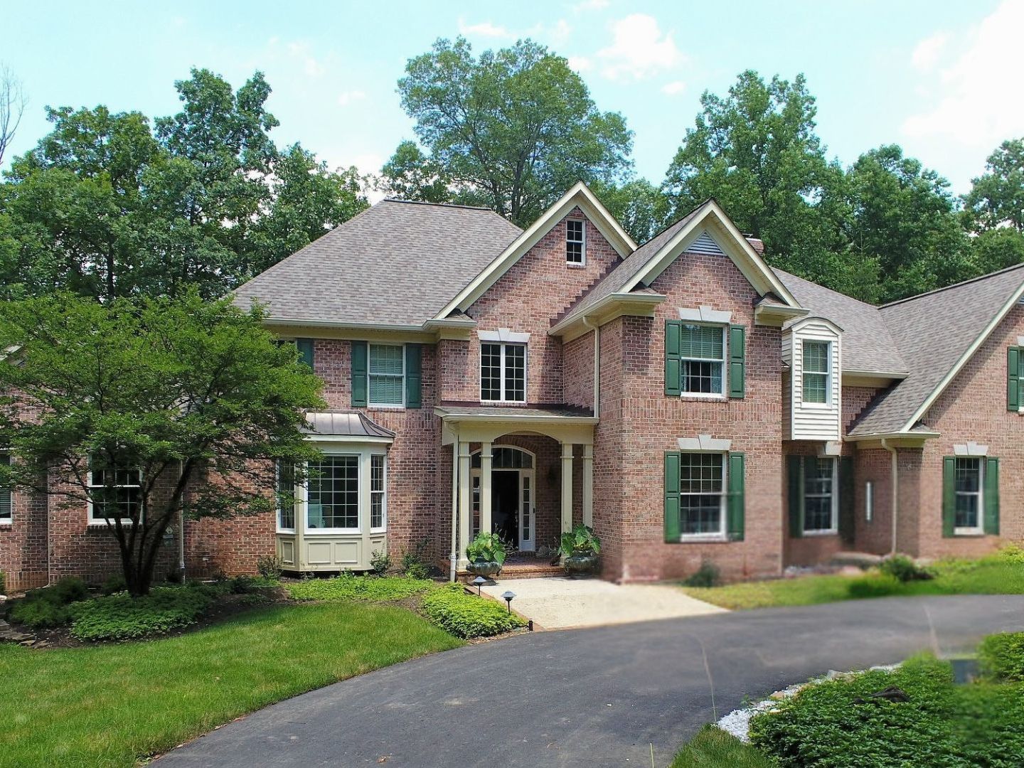 A large brick house with green shutters and a driveway