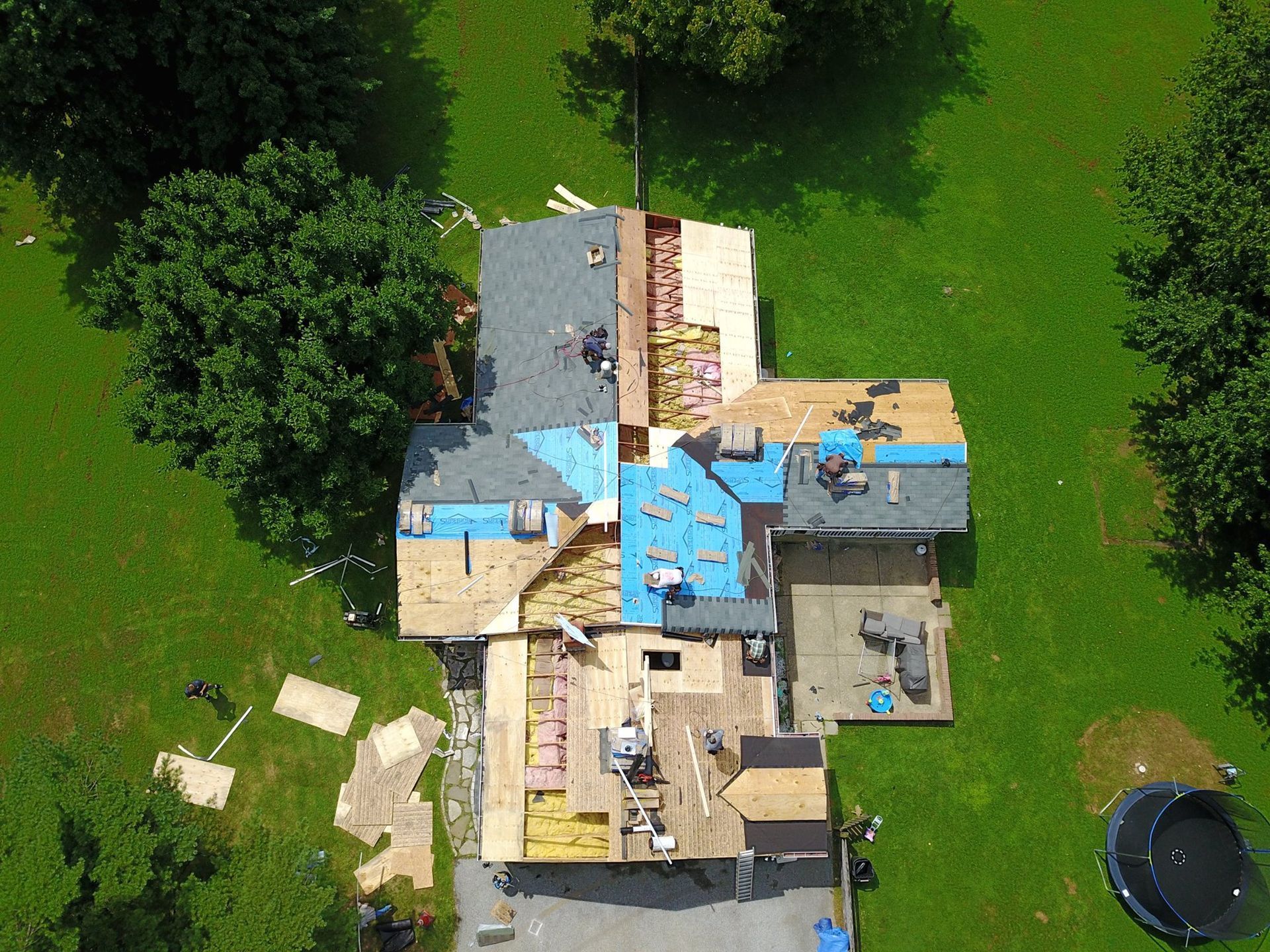 Roof replacement in progress; workers on roof; exposed wood, tarps, and new shingles.