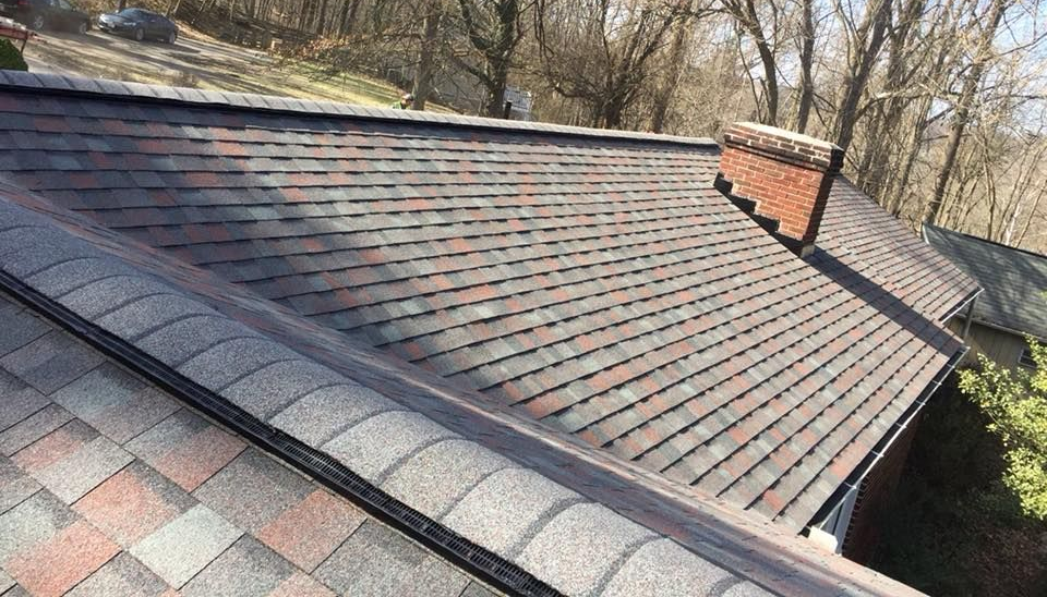 Roof with dark gray and red asphalt shingles and full ridge vent, with a brick chimney and gutter.