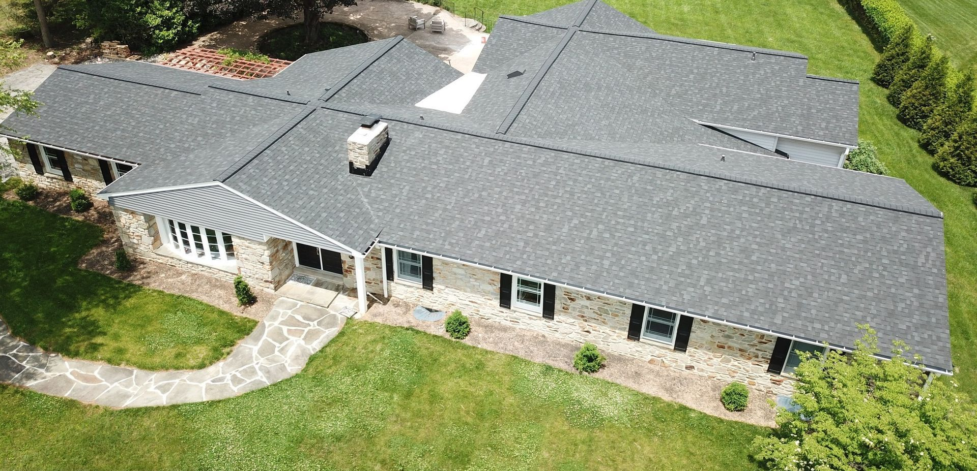 Overhead view of a stone-faced house with a dark gray architectural roof installed by Four Seasons
