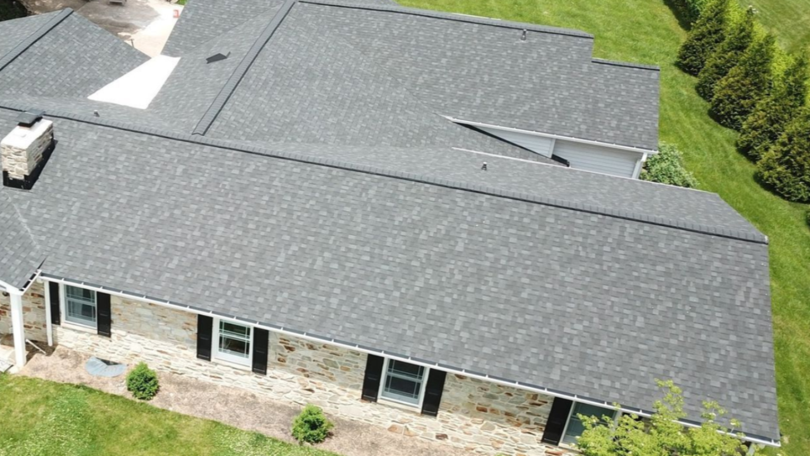 Overhead view of a house with a gray shingled roof, windows, and surrounding green lawn.
