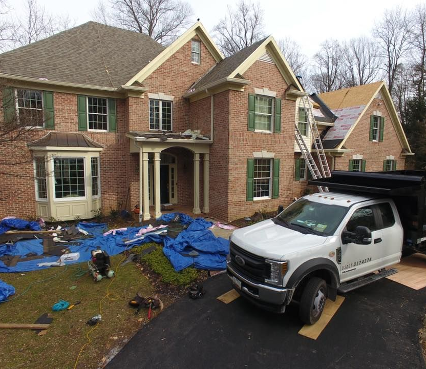 House with ongoing roof replacement. White truck, ladder, blue tarps, green shutters.