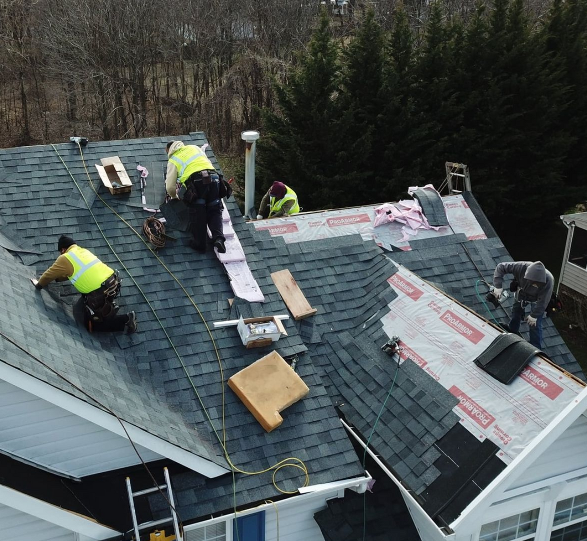 Roofers working on a house roof. Shingles, tools, and safety vests visible.
