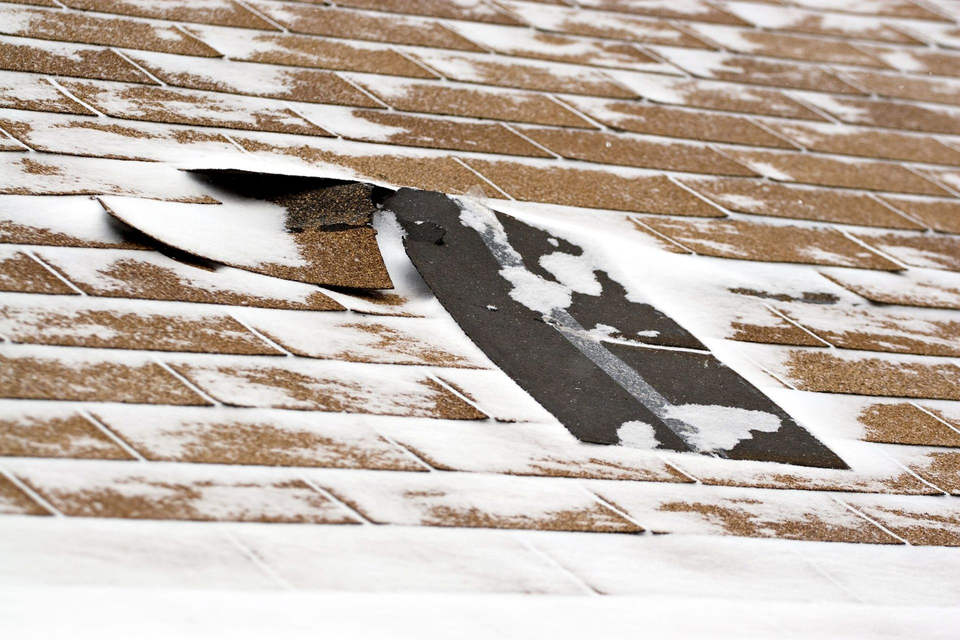 Damaged asphalt shingle roof with a hole, covered in snow.