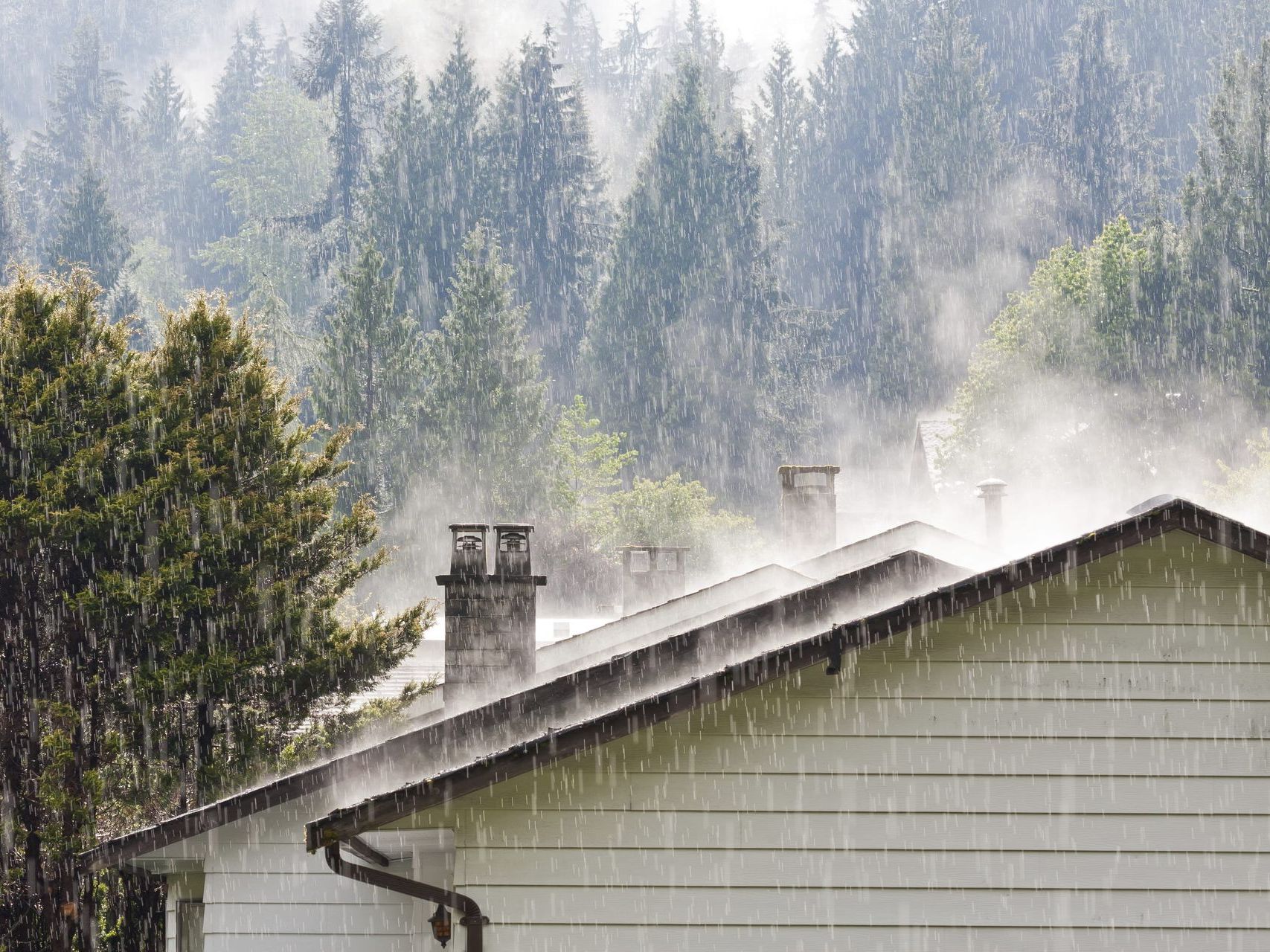 Heavy rain falling on a residential roof, stressing the shingles and gutters | Four Seasons Roofing