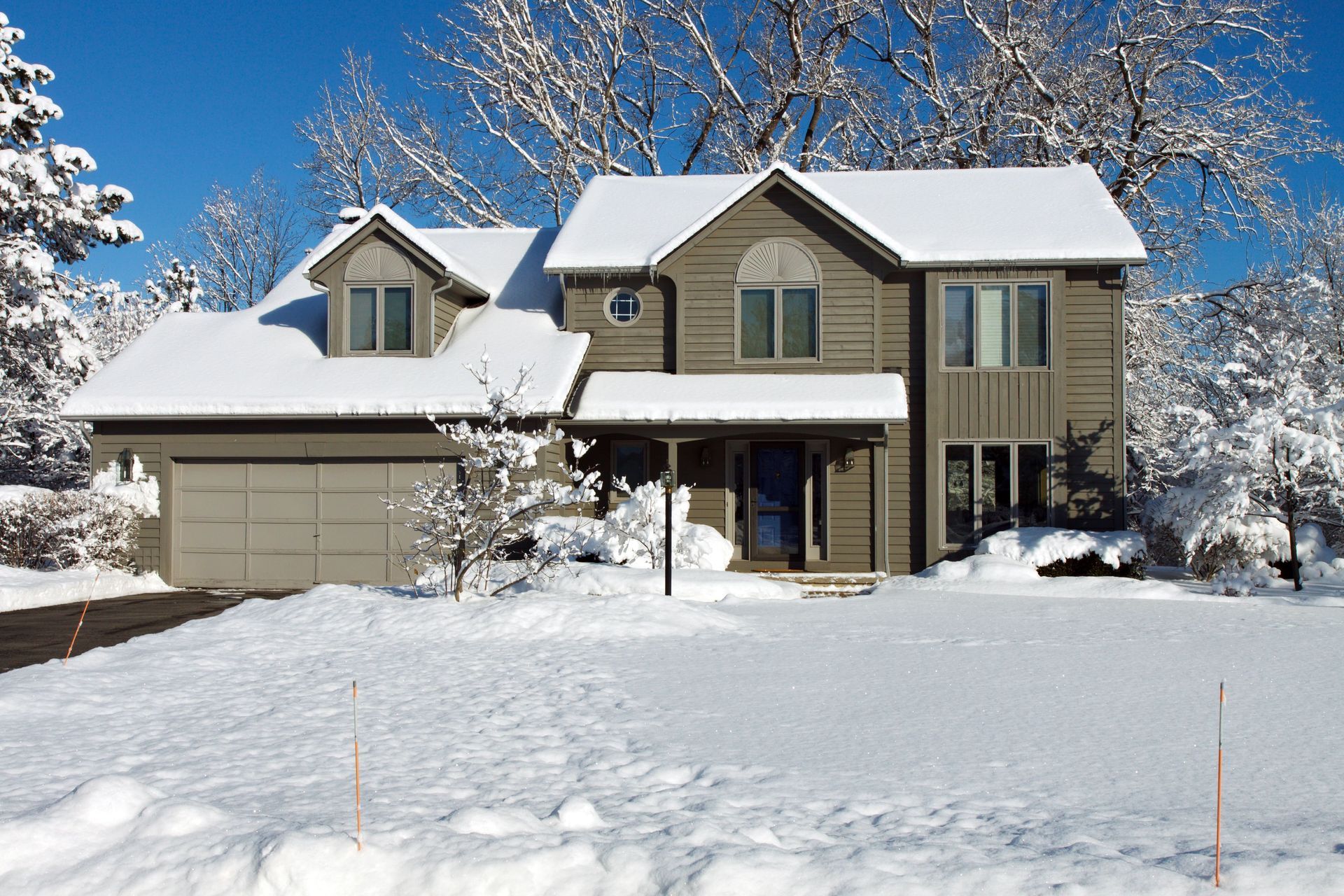 Snow-covered house on a sunny winter day, with a garage and porch under a clear blue sky.