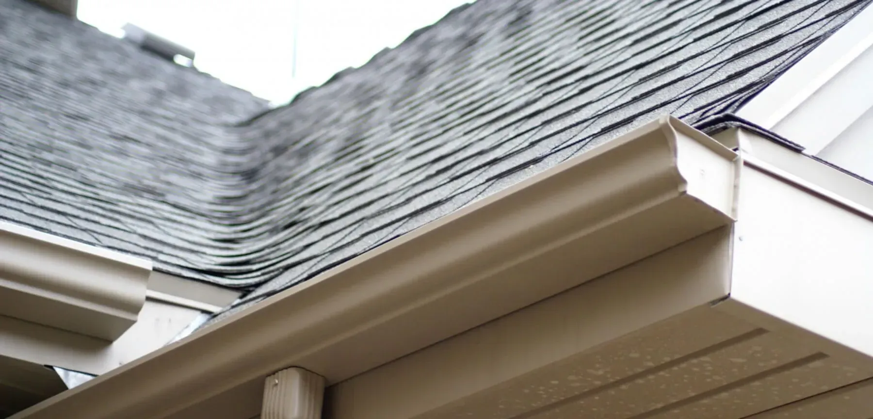 Gray roof with tan gutters on a beige house.