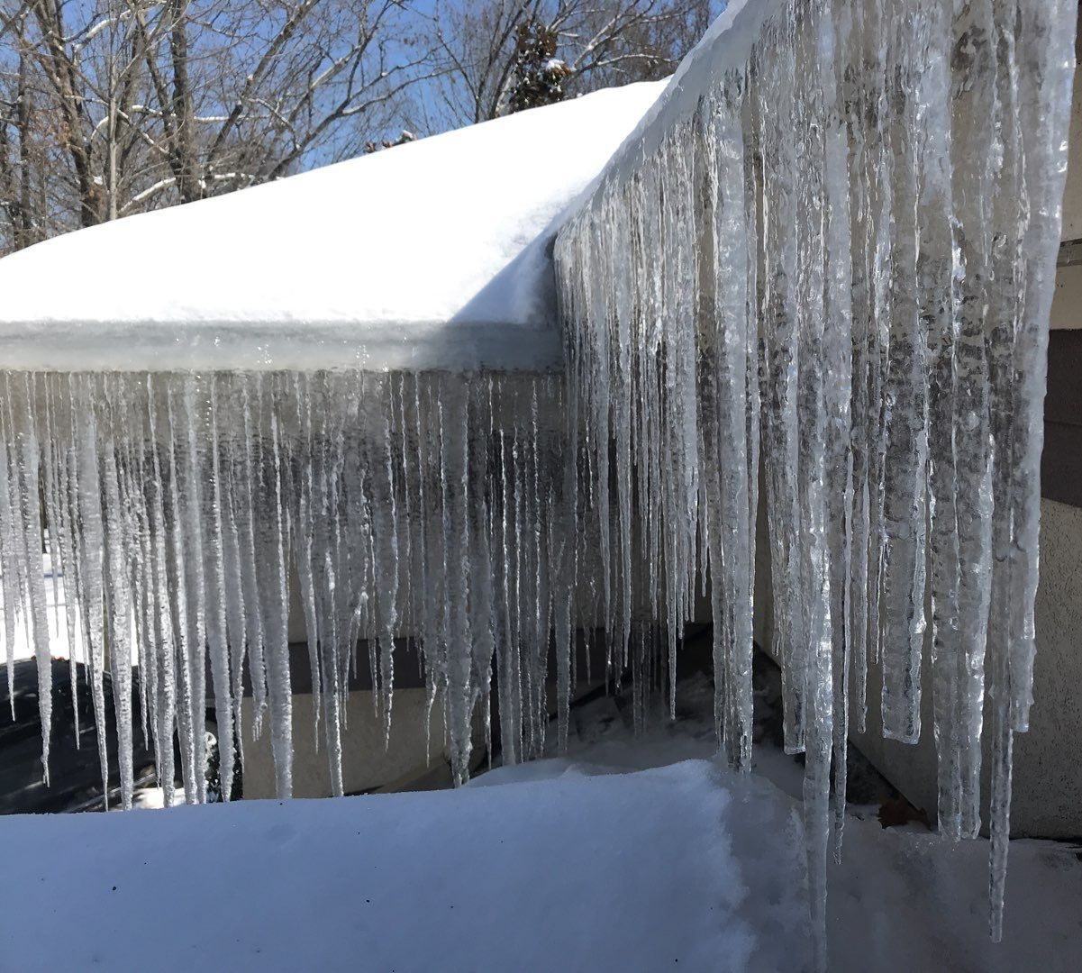 Icicles hanging from a snow-covered roof gutter. Bright sunlight.