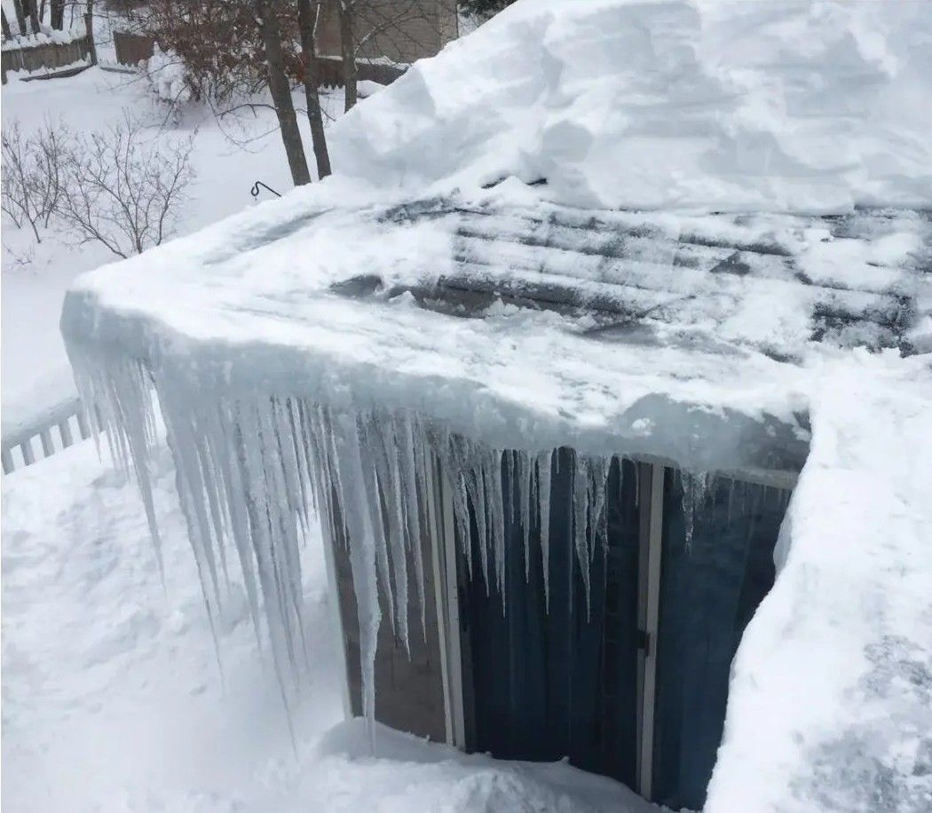 Snow-covered roof with large ice dam and icicles hanging down, creating a hazard.