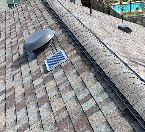 A roof with brown and tan shingles, a solar panel, and multiple vents.