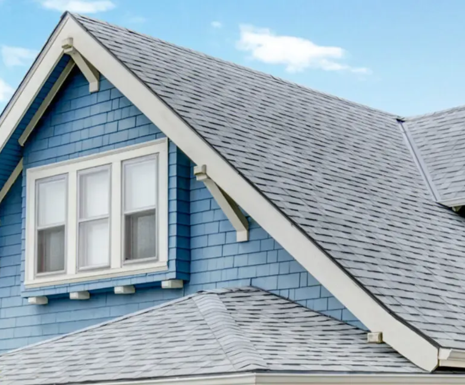 A blue-shingled house exterior featuring a prominent gable roof with grey shingles and a three-pane window.