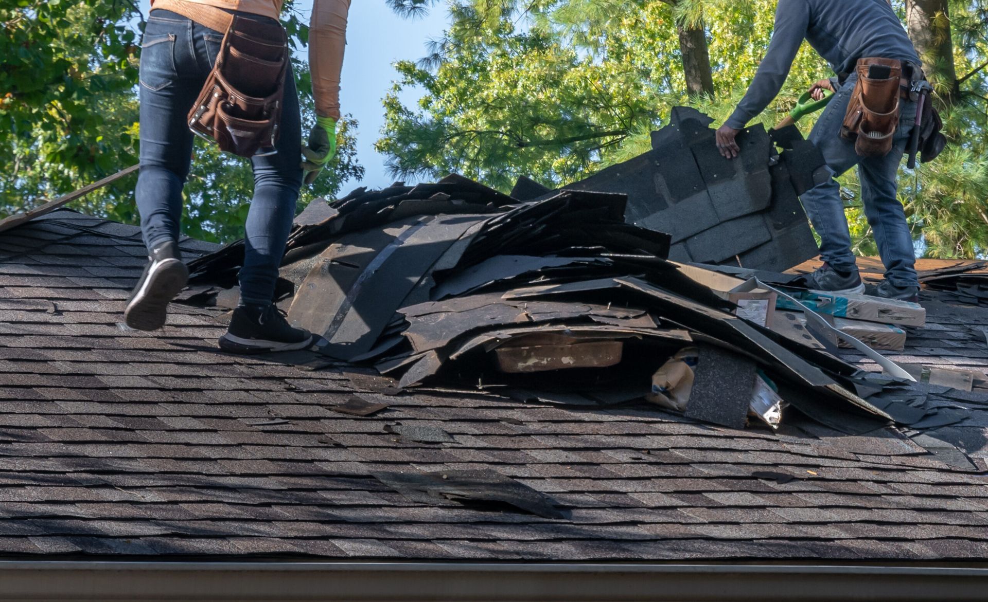 Two local roofers workers stripping old shingles off a residential roof.