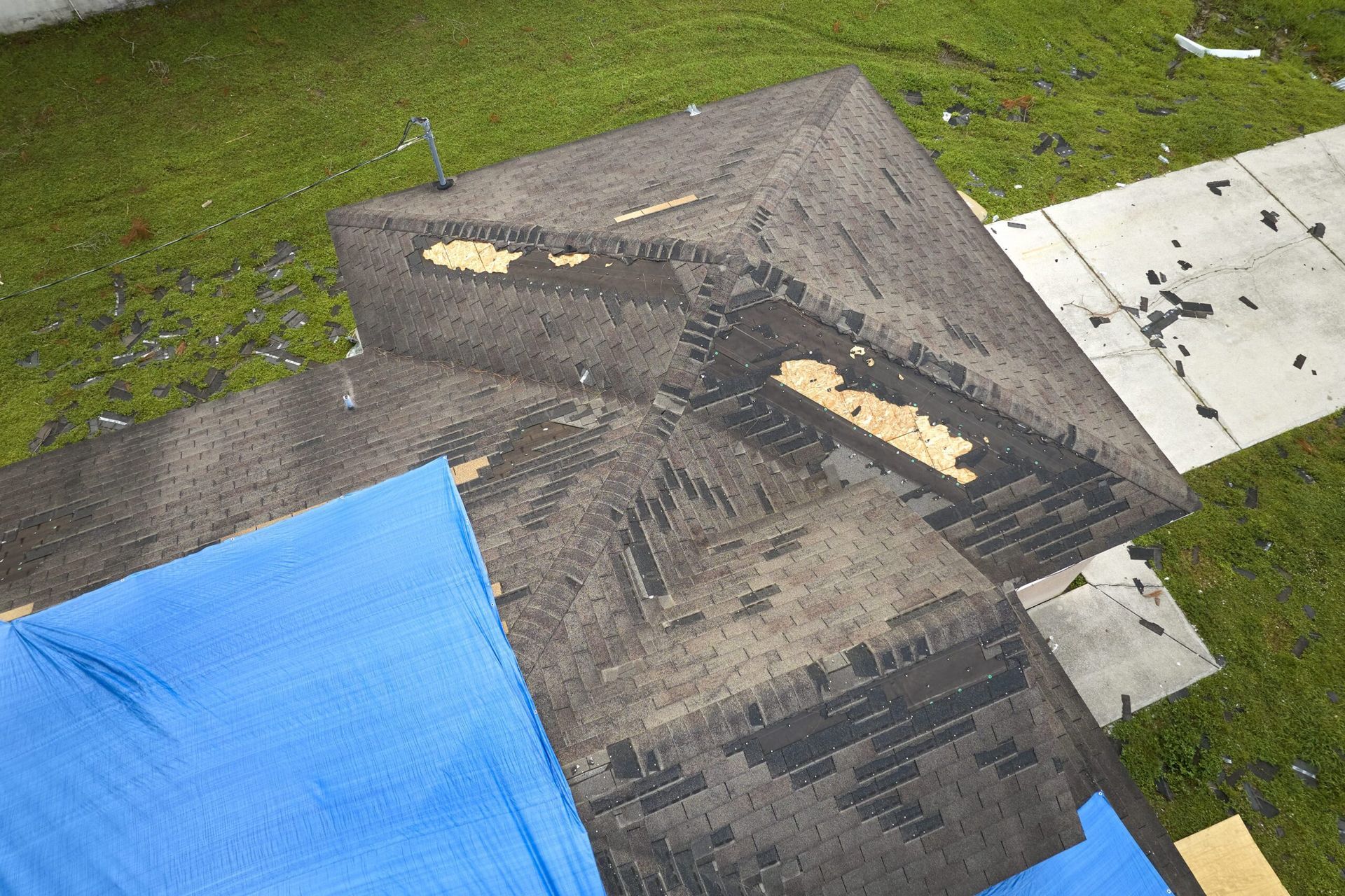 Severely storm-damaged roof in Maryland with emergency tarp covering exposed section after heavy summer storms