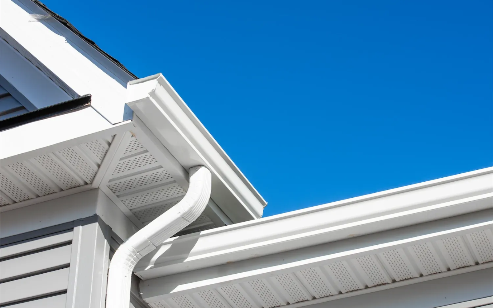 White gutters and siding on a house against a bright blue sky.