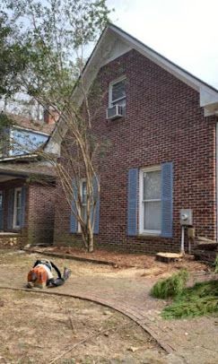 A man is laying on the ground in front of a brick house with blue shutters.