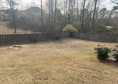 A backyard with a fence and trees in the background.