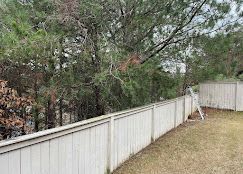 A white fence surrounds a yard with trees in the background.