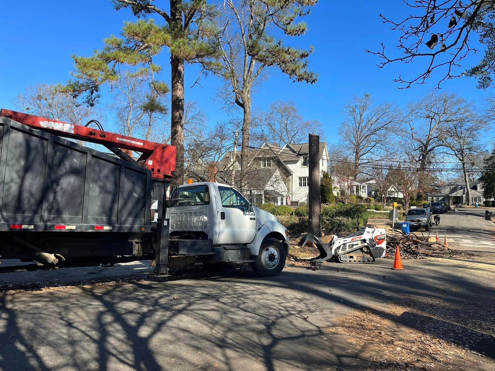 A white truck with a crane attached to it is parked on the side of the road.