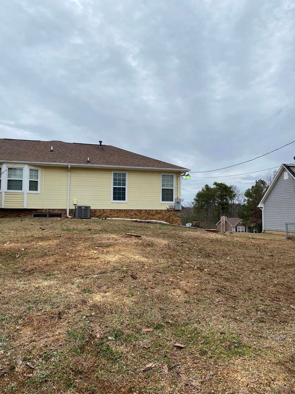 A yellow house is sitting on top of a dirt hill next to a white house.