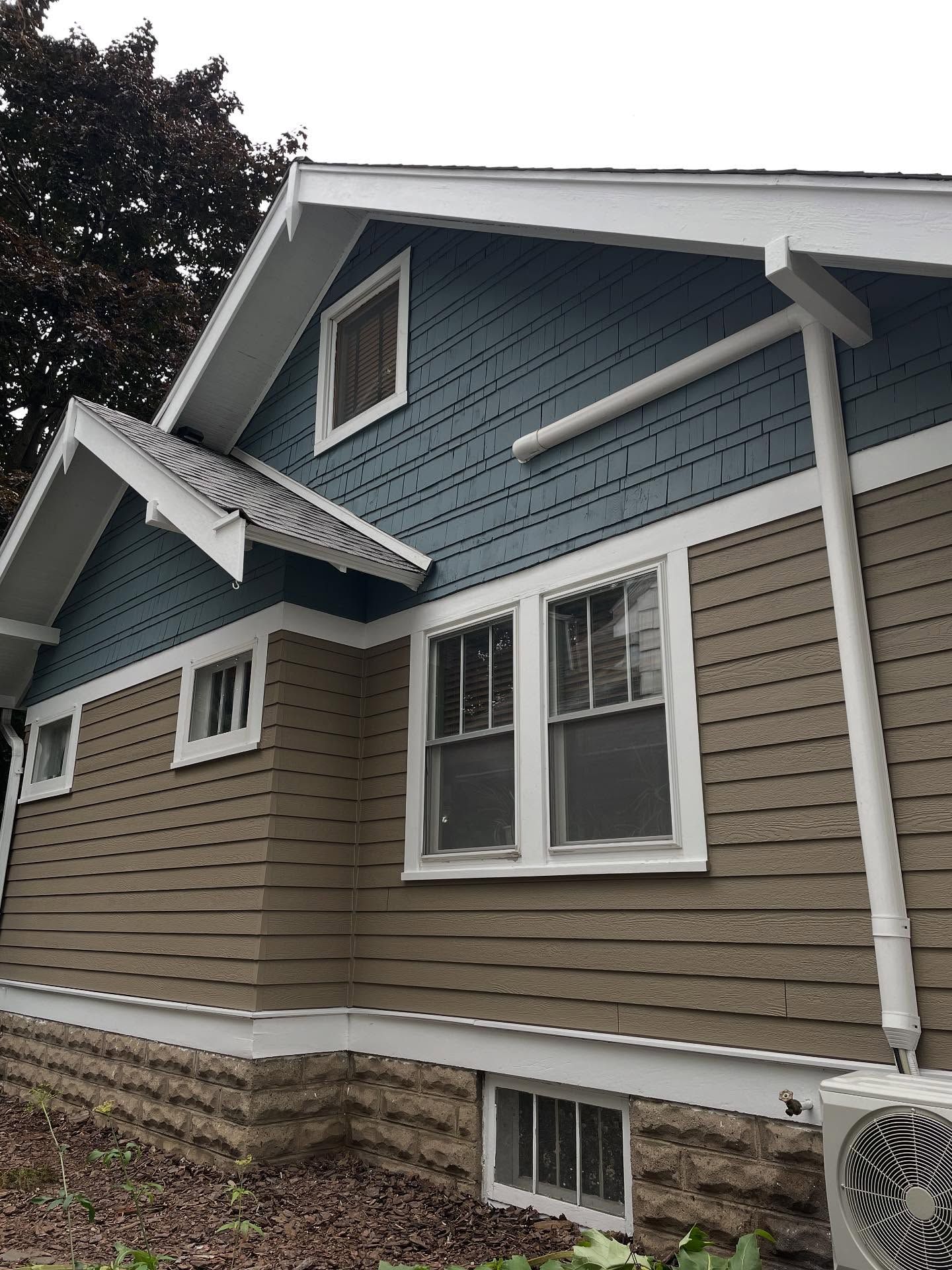 Side view of a house with blue and brown siding, white trim, and a small air conditioner unit.