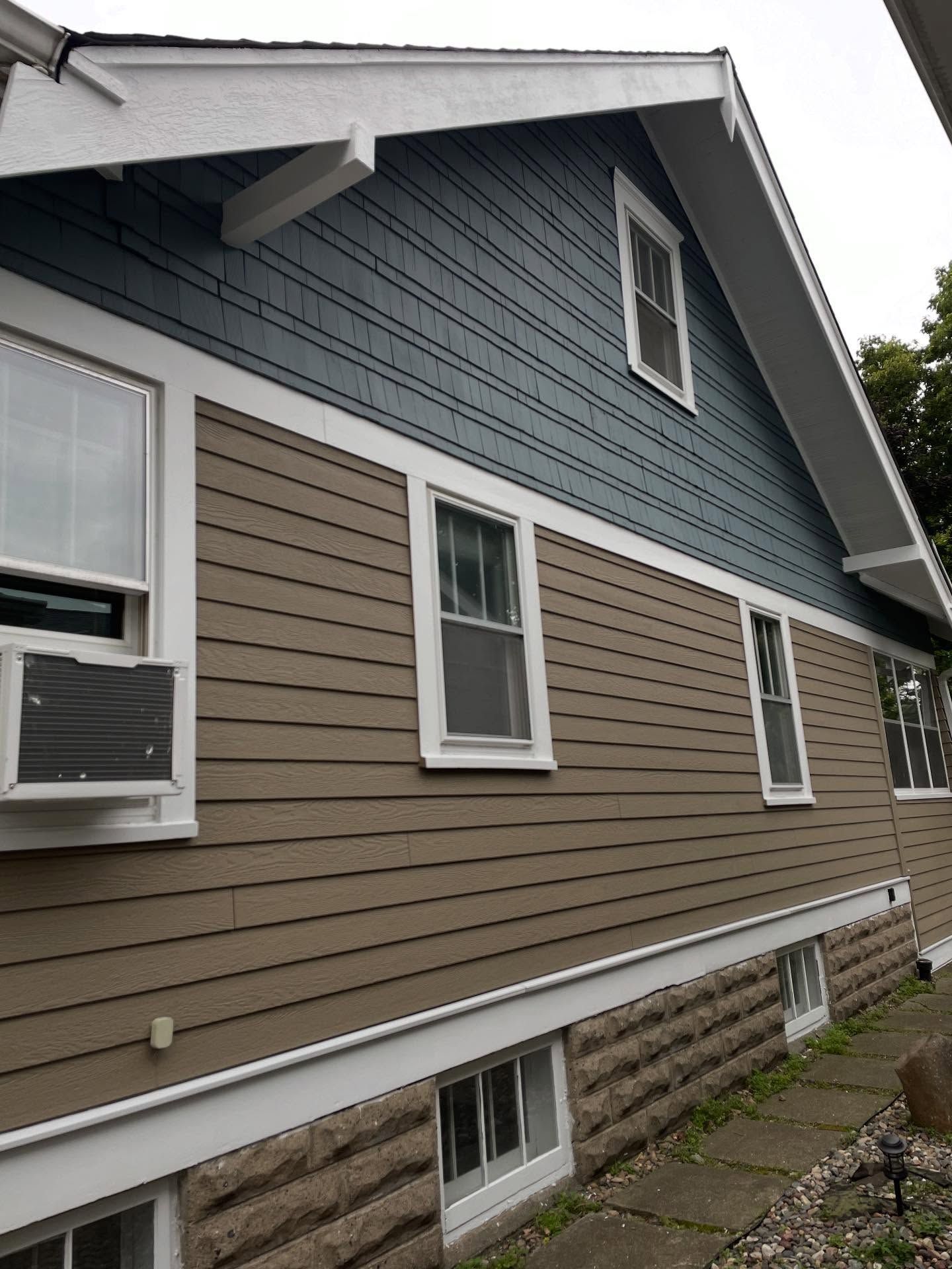 Two-story house with blue shingle siding on top and brown horizontal siding on the bottom. Windows are trimmed in white.