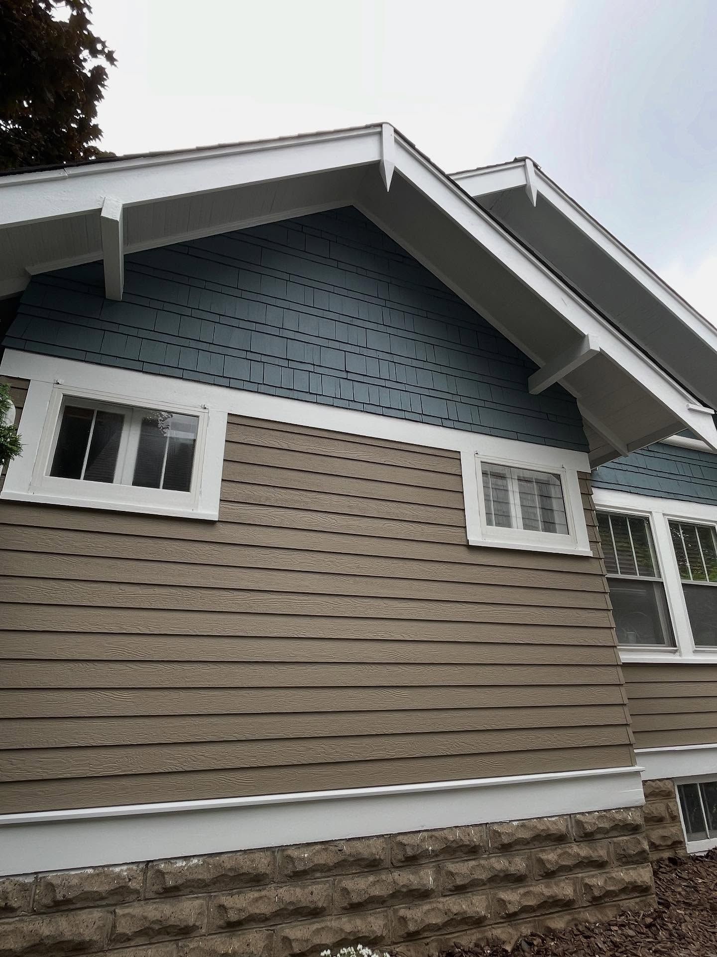 Blue and brown house exterior with white trim, two windows, and stone foundation.