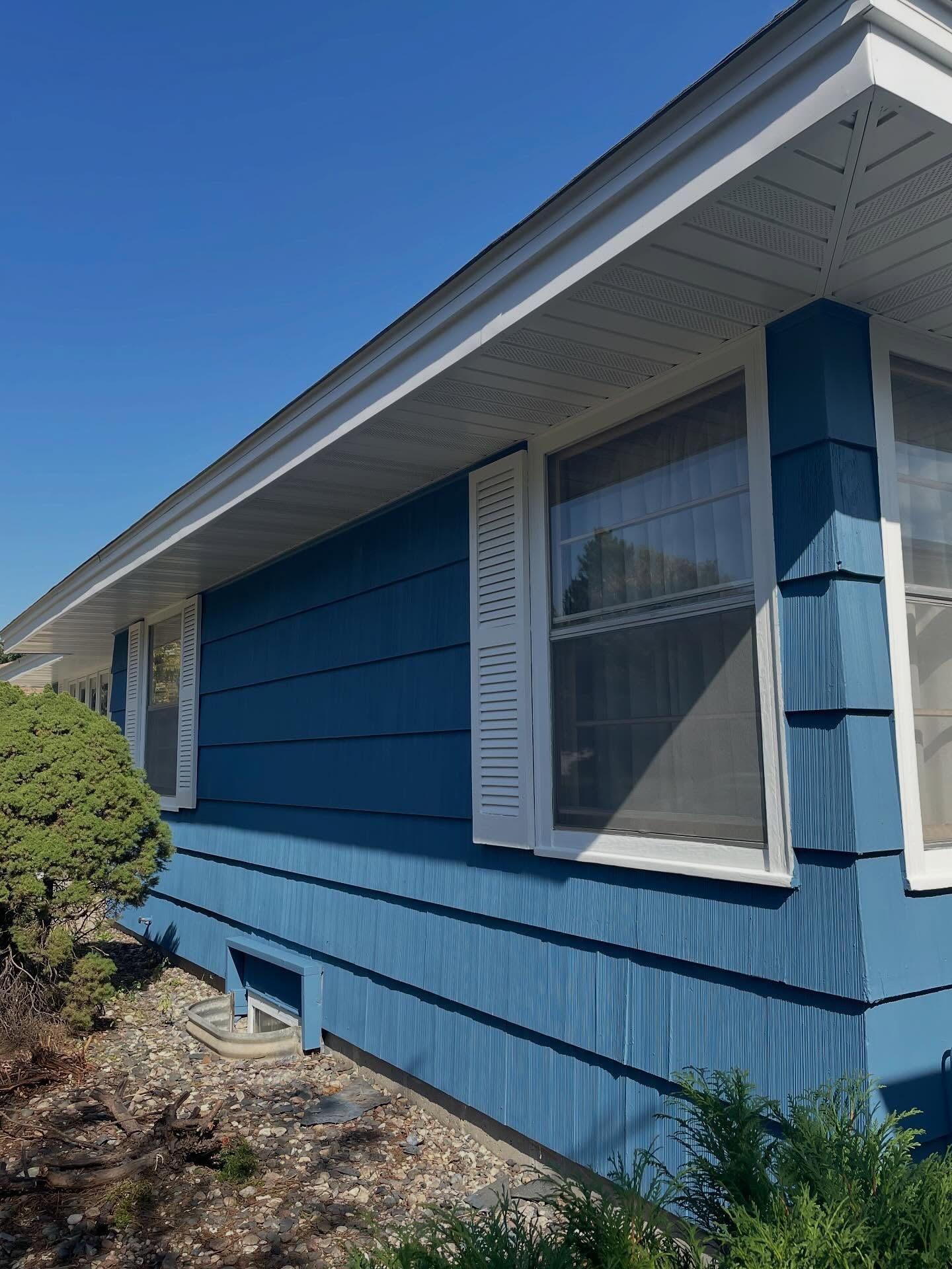 Blue house exterior with white trim, shutters, and bright blue sky.