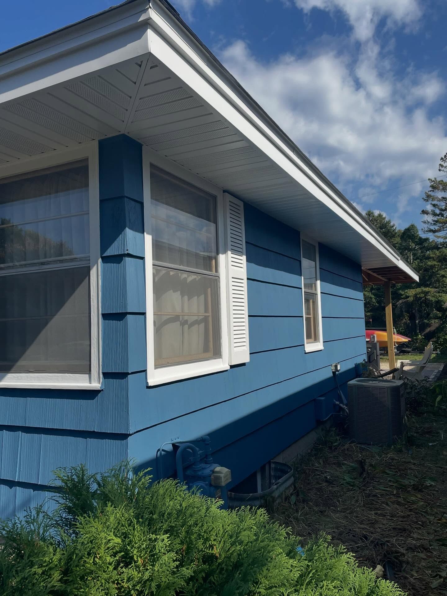 Blue house with white trim, windows, and shutters against a cloudy sky.