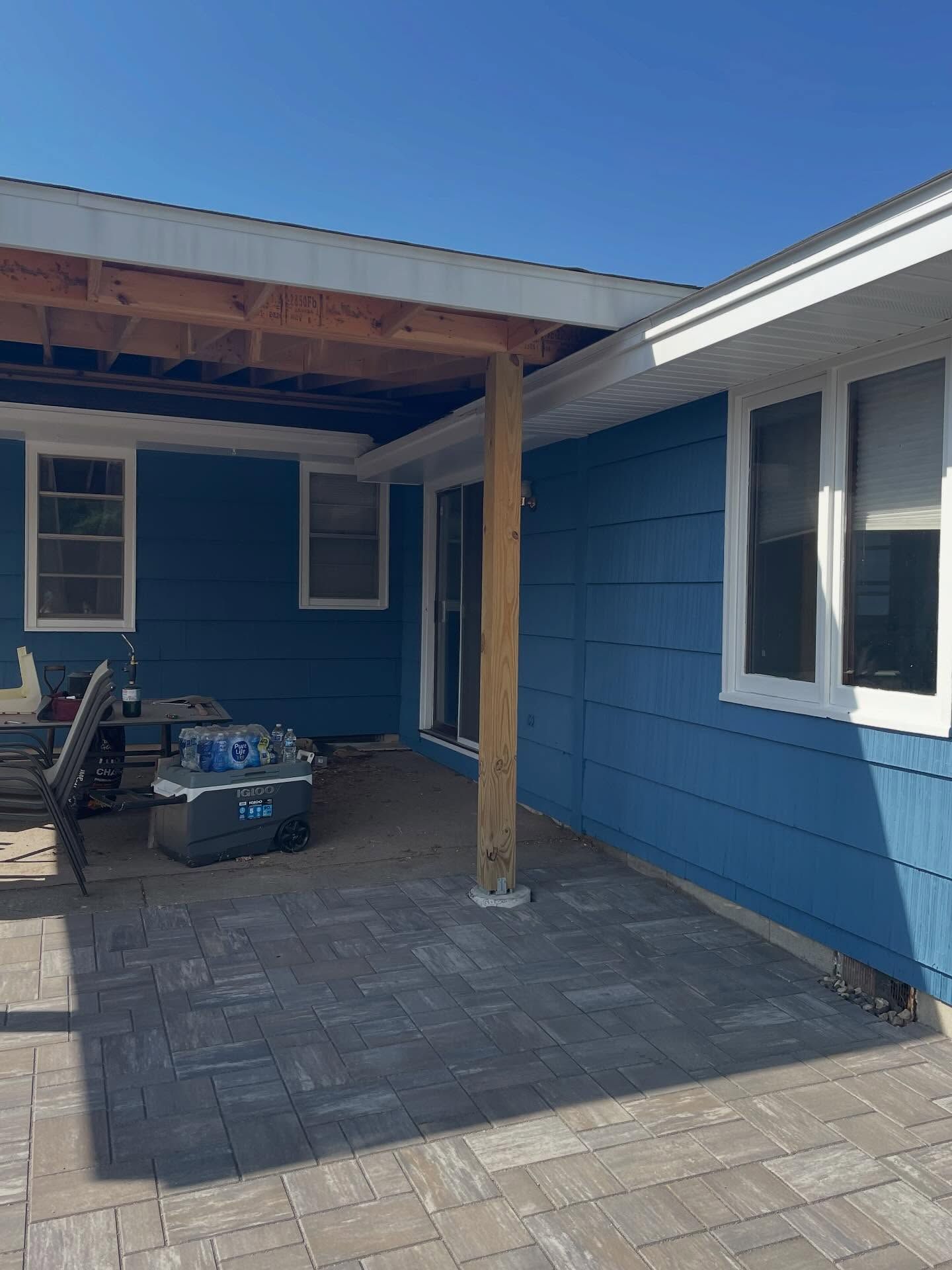 Blue house with a partially constructed patio cover. Pavers make up the patio floor.