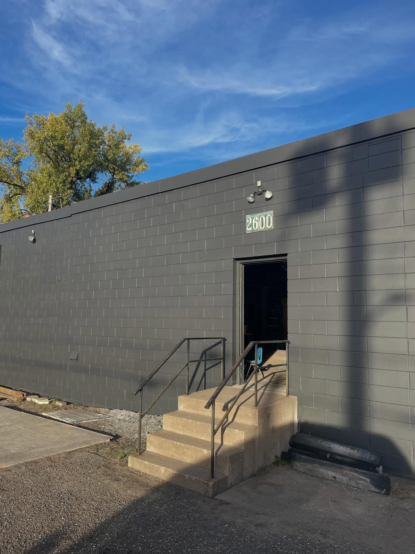 Gray building with an open doorway, steps, and handrails. The address 