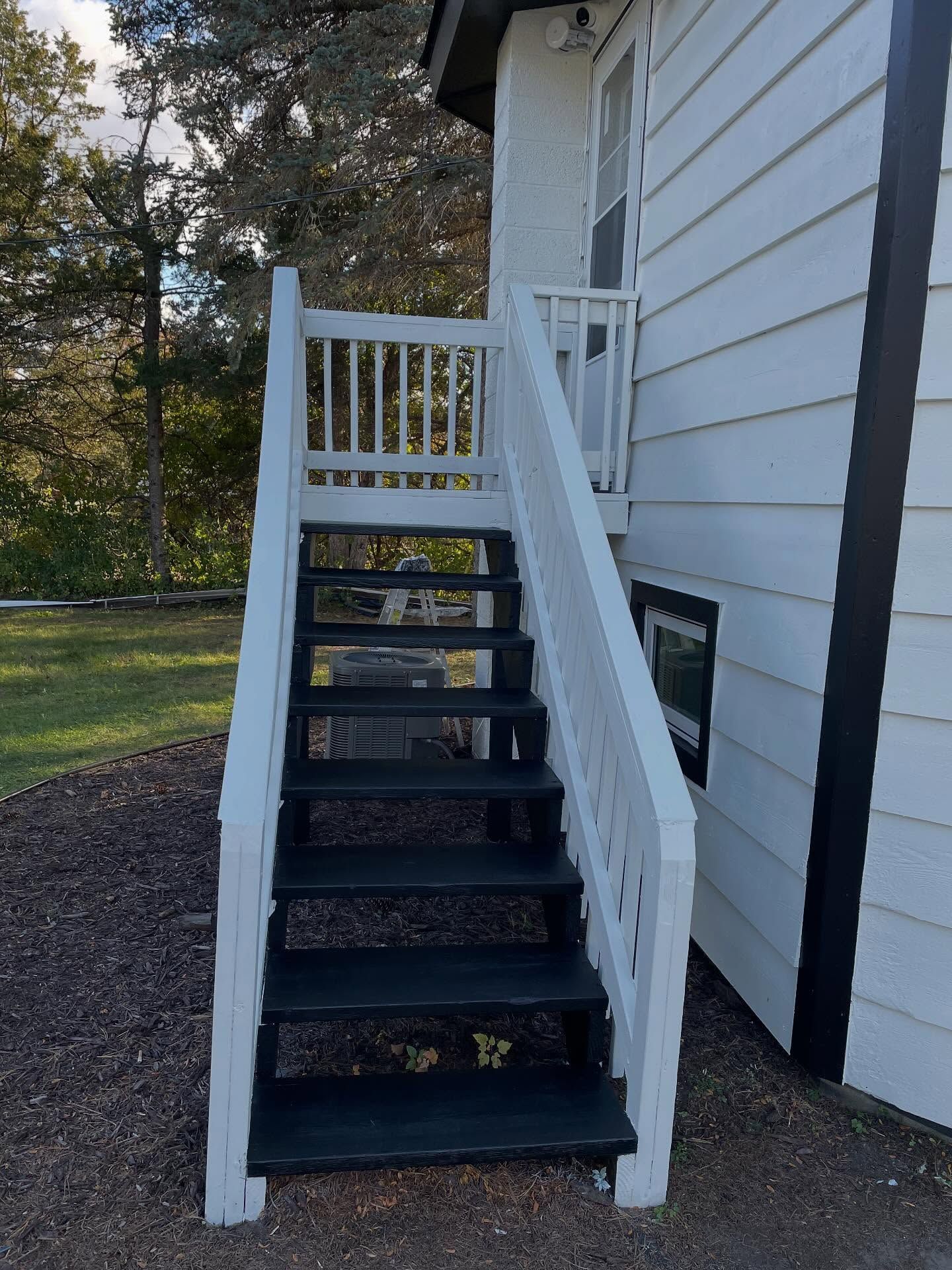 Exterior staircase with white railing, black steps, leading to a white building with a window.