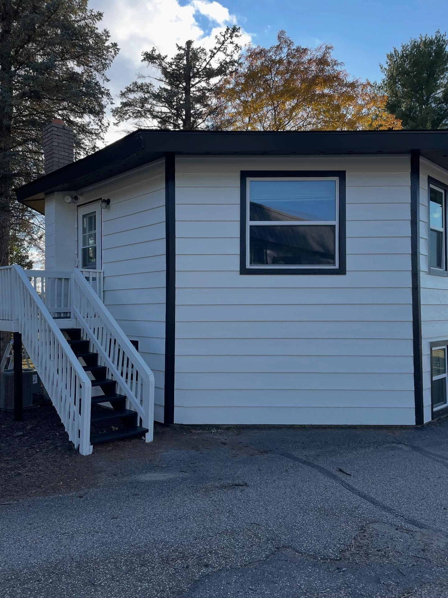 White house with black trim, a staircase, and a window reflecting a sky.