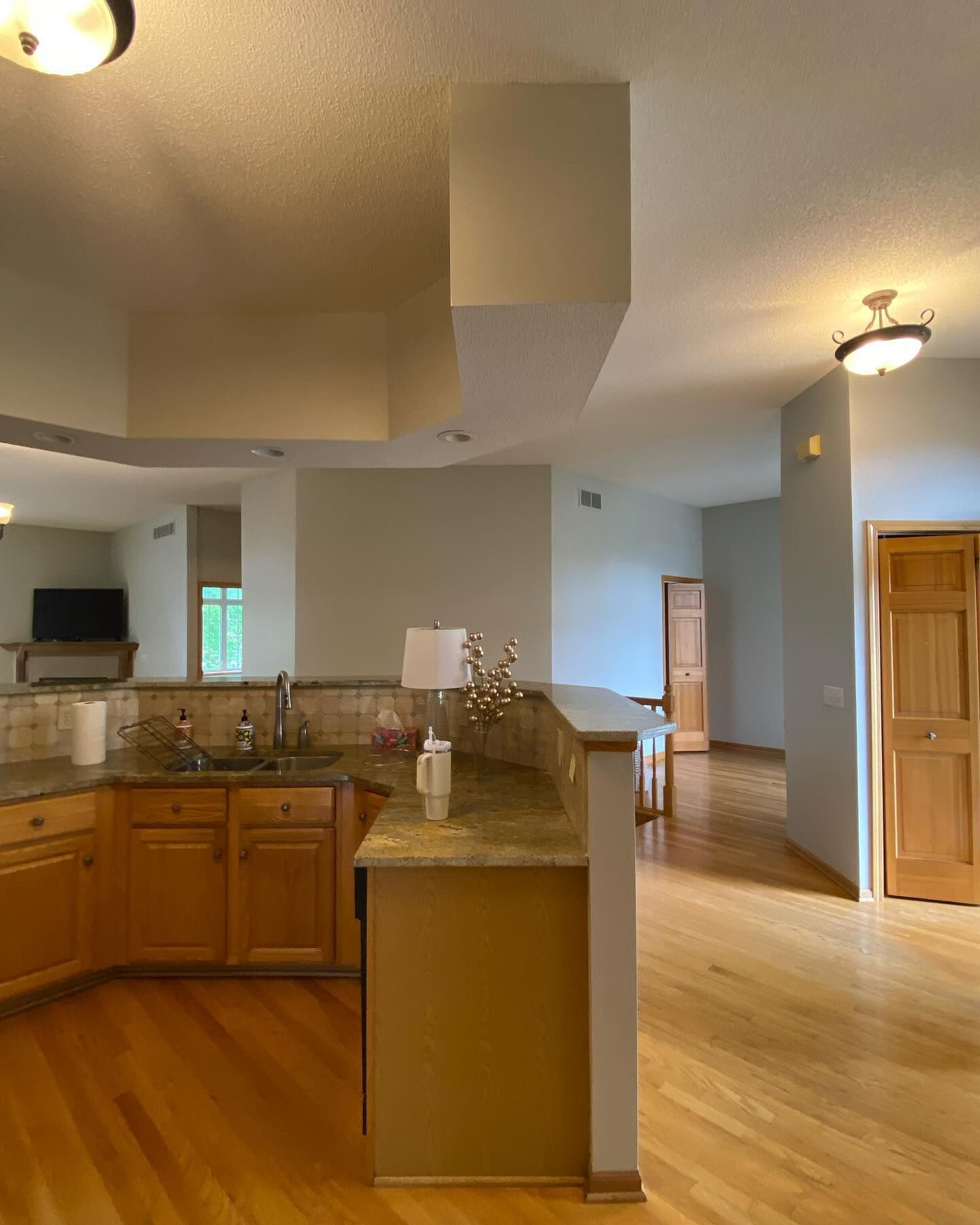Kitchen with wood cabinets, granite countertops, and light-colored walls and ceiling, connected to a living area with hardwood floors.