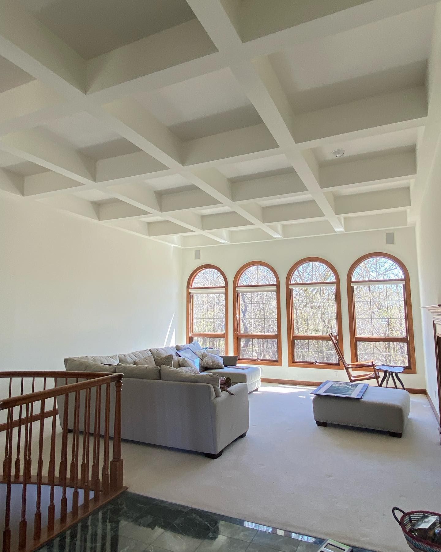 A spacious living room with a coffered ceiling, large arched windows, and a light gray sectional sofa.