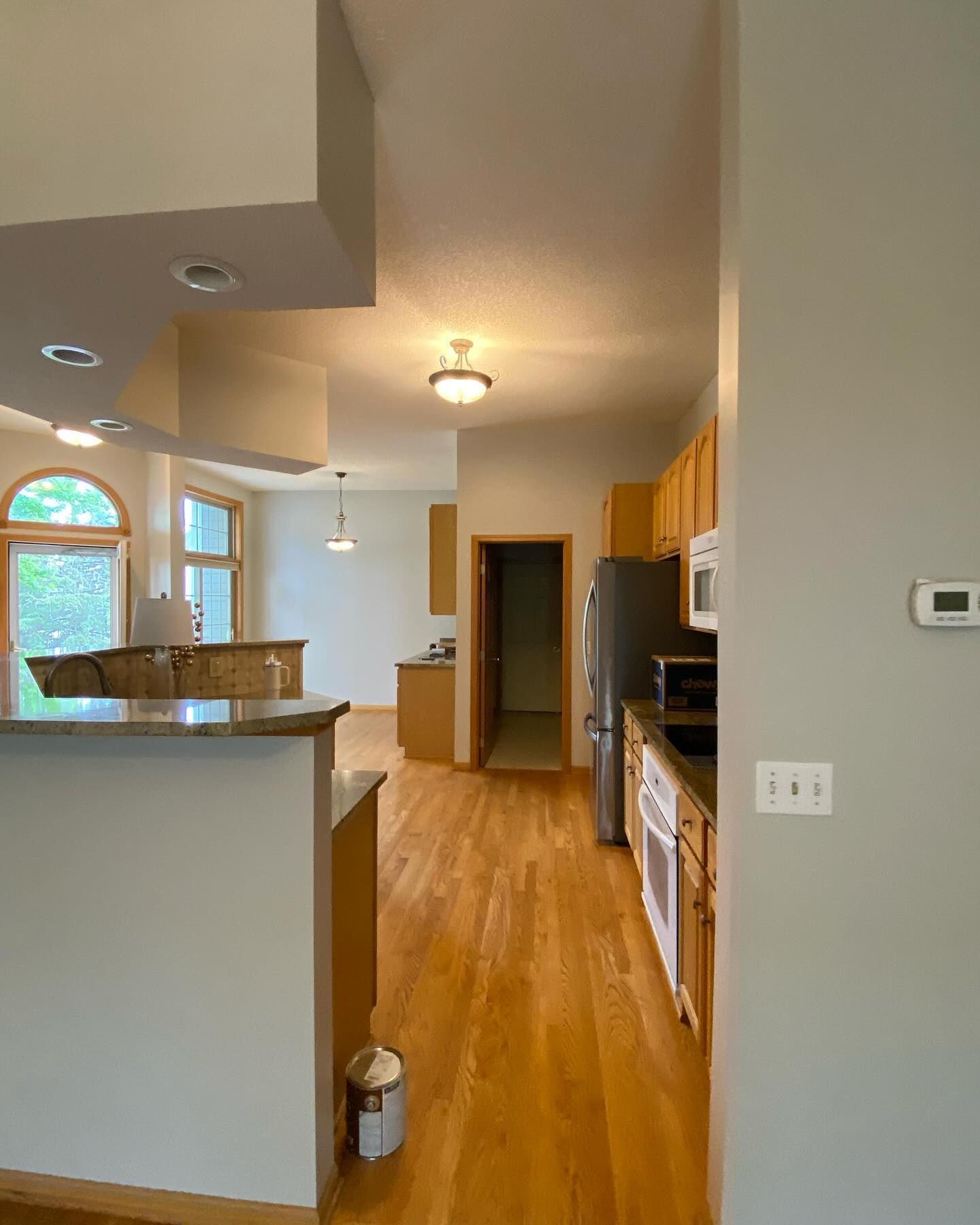An open kitchen and dining area with wood floors and light-colored cabinetry and walls. The kitchen contains appliances.
