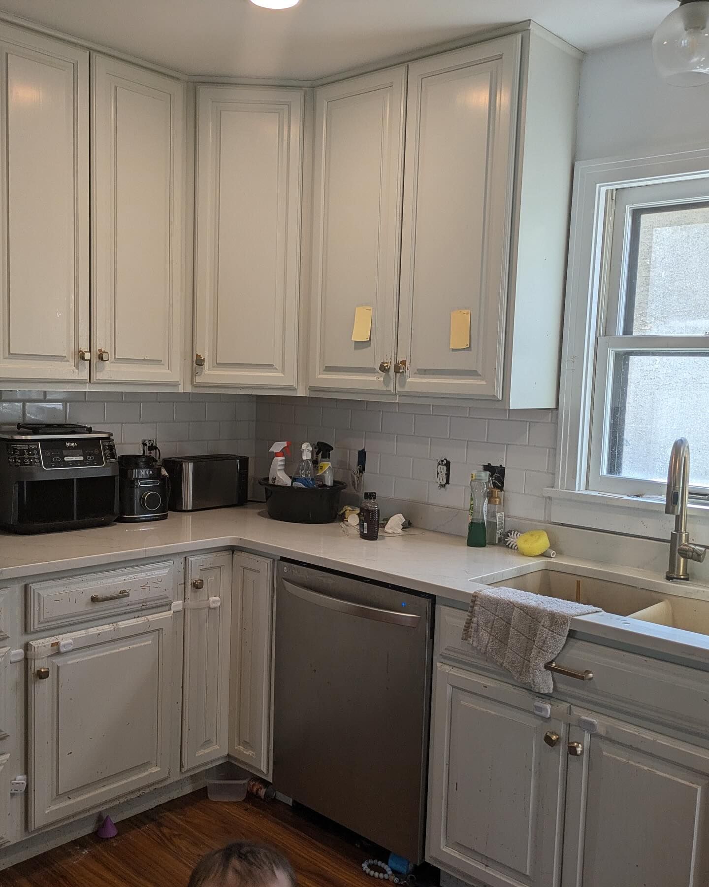 A kitchen with white cabinets, stainless steel appliances, and a white countertop. The walls have white subway tile.