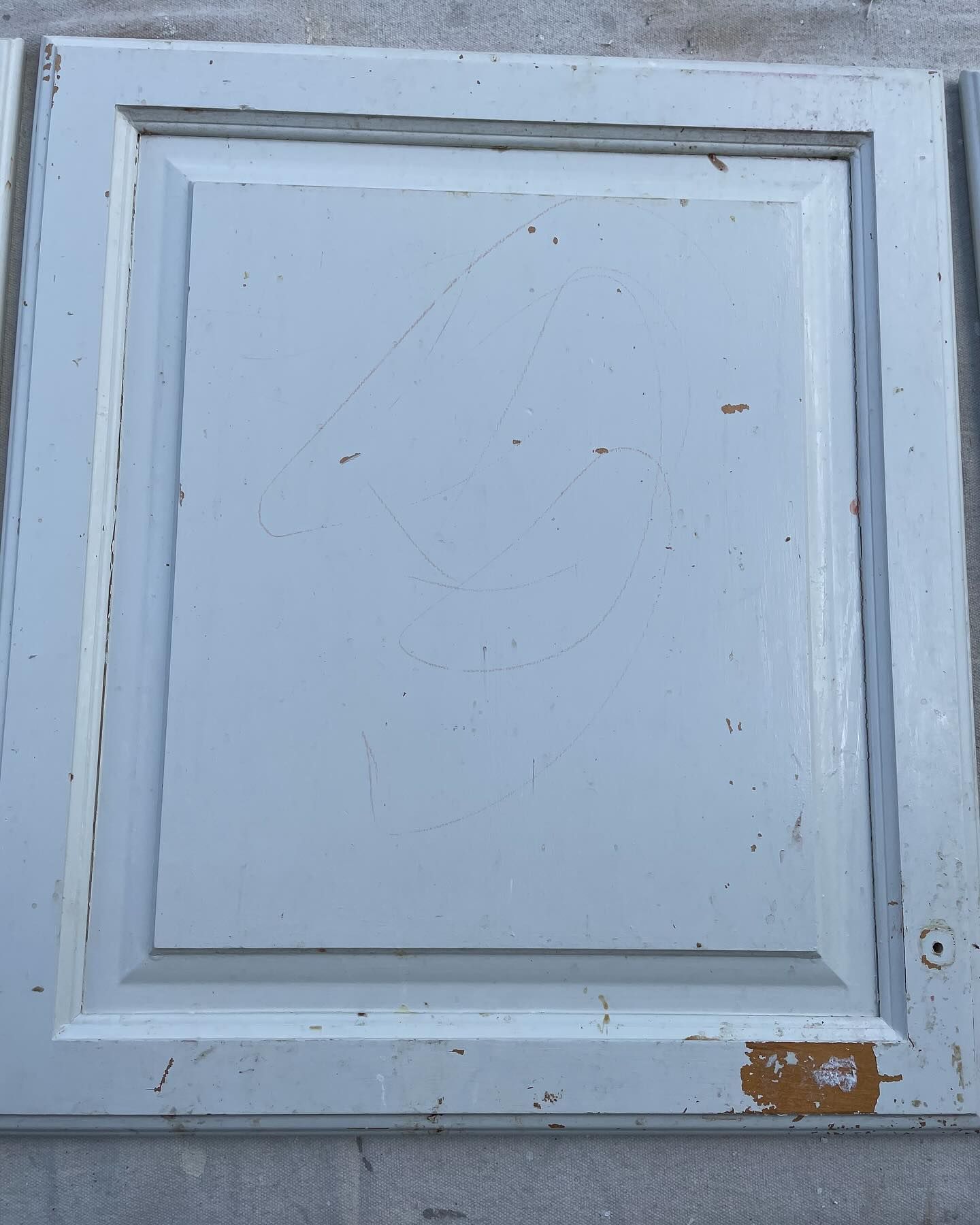 Close-up of a white painted cabinet door with a recessed center panel and some scratches and paint chips.