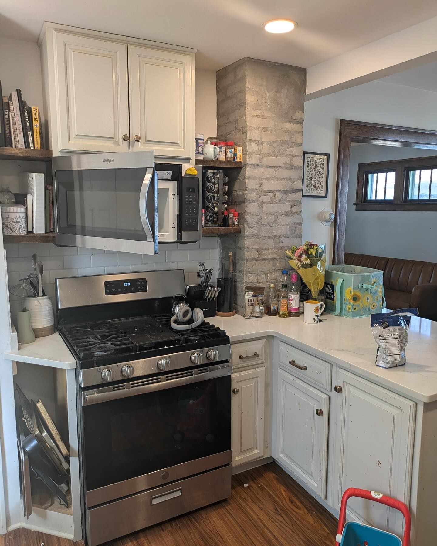 A kitchen with white cabinets, stainless steel appliances, a brick accent wall, and a counter with gifts.